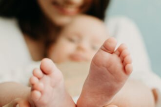 Health Insurance For Newborn Babies. Life Insurance for New Baby. Mother holding in hands feet of newborn baby. Baby feet in parent hands