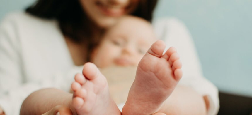 Health Insurance For Newborn Babies. Life Insurance for New Baby. Mother holding in hands feet of newborn baby. Baby feet in parent hands